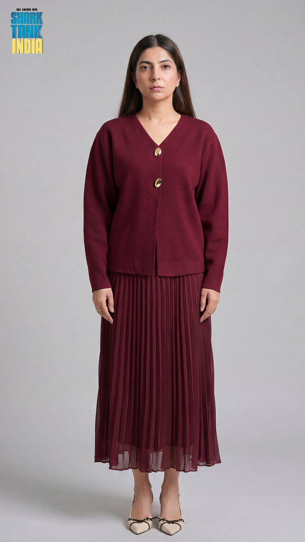 Woman wearing a burgundy outfit with a cardigan and pleated skirt on a gray background
