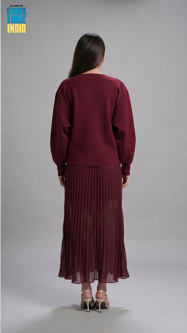 Woman wearing a maroon outfit with a pleated skirt on a gray background