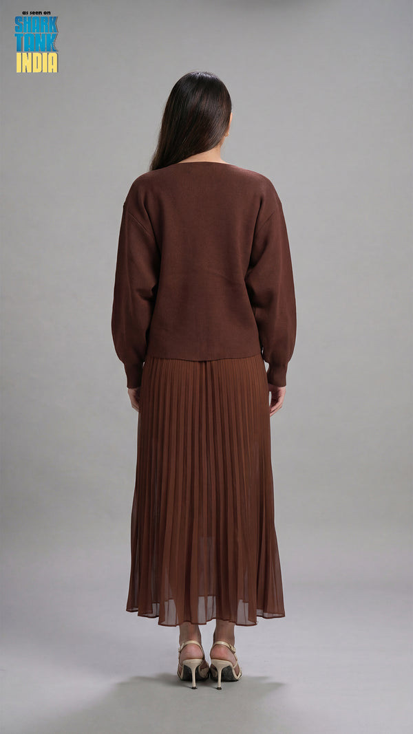 Woman wearing a brown outfit with a pleated skirt on a gray background