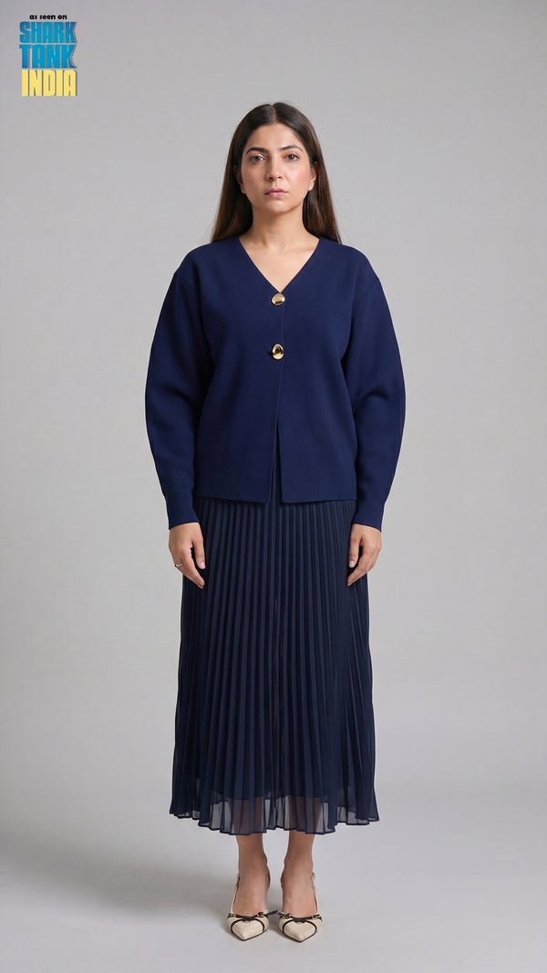 Woman wearing a navy blue cardigan and pleated skirt on a gray background