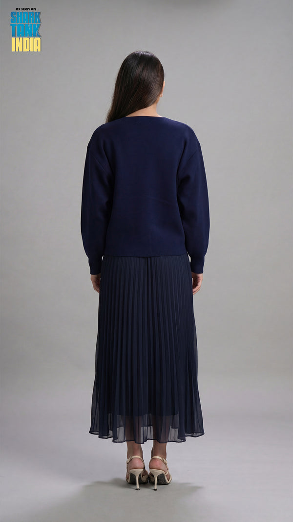 Woman wearing a navy blue sweater and pleated skirt on a gray background