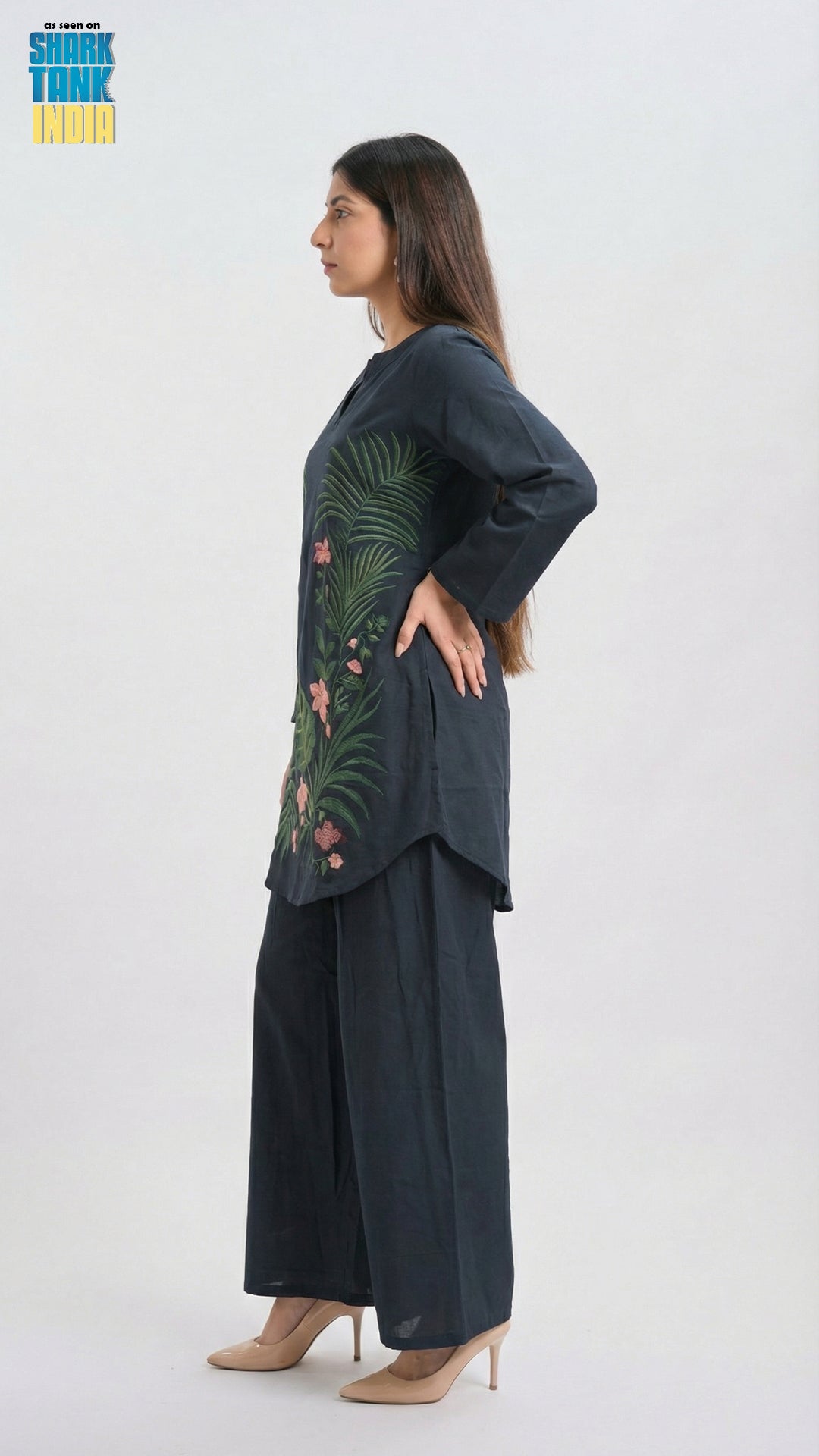 Woman wearing a dark green embroidered top and black pants on a white background