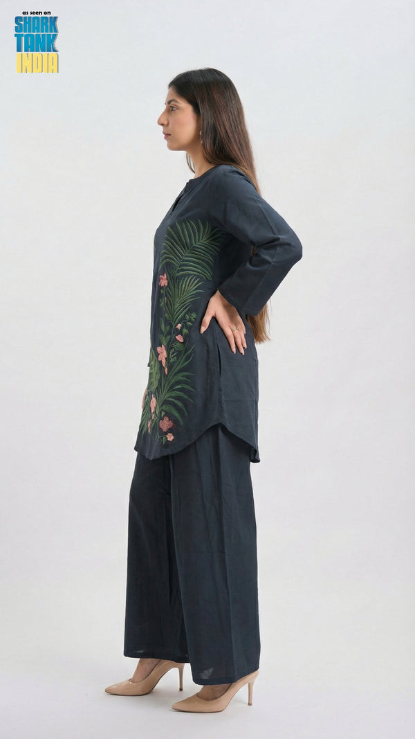Woman wearing a dark green embroidered top and black pants on a white background