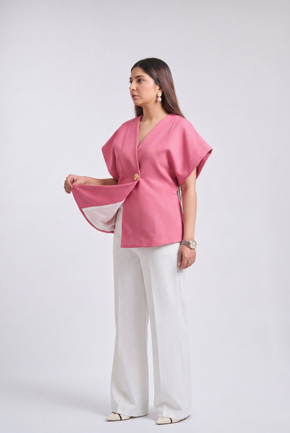 A woman modeling a pink short-sleeve wrap-style top with white wide-leg trousers, standing against a light gray studio background.