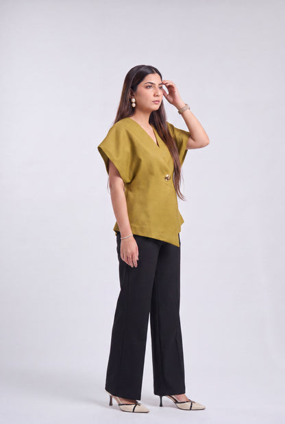 A woman modeling a mustard yellow short-sleeve top with black wide-leg pants and beige heeled sandals, standing against a light gray studio background.
