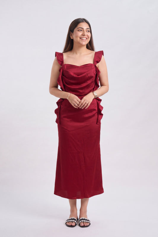 A woman modeling a sleeveless, deep red midi dress with ruffled shoulder details and a draped bodice, standing against a plain light gray background.