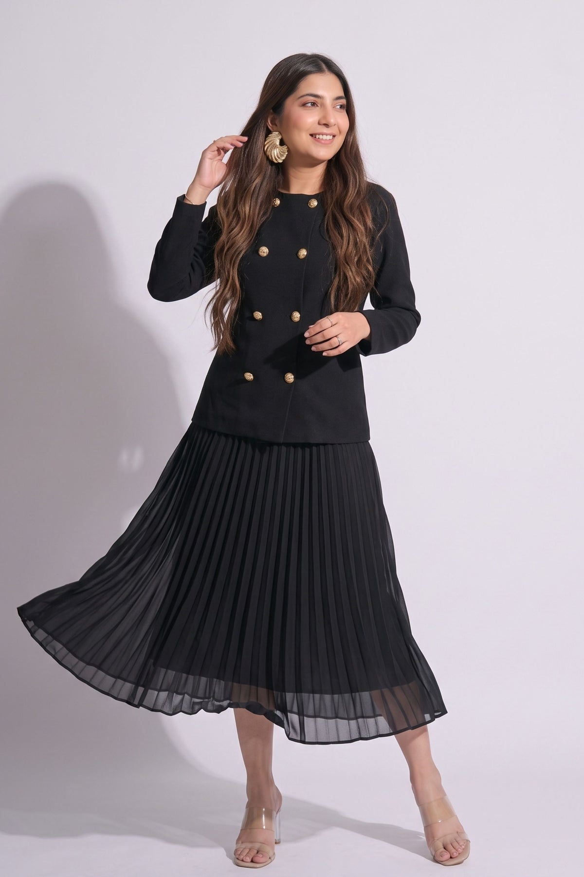 Woman wearing a black outfit with a jacket and pleated skirt on a white background