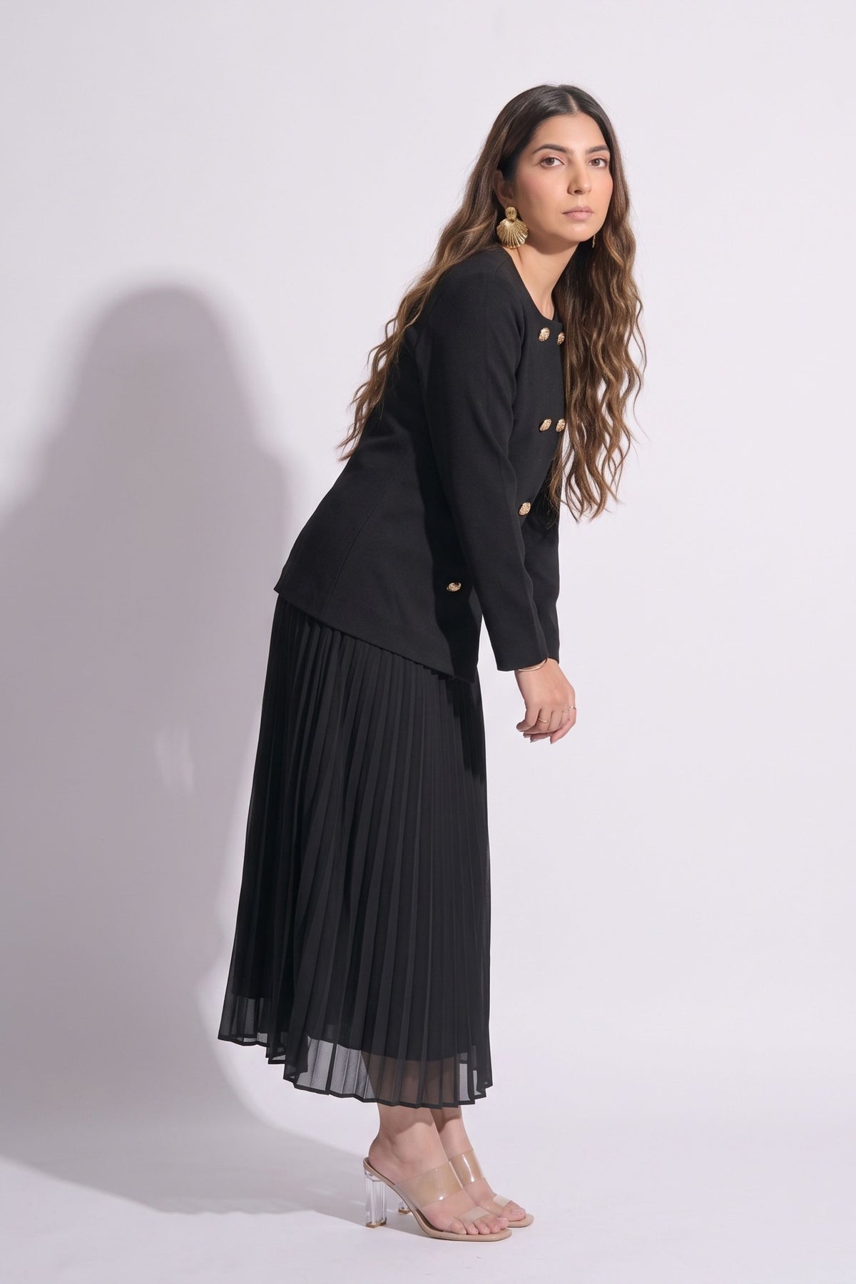 Woman wearing a black outfit with a jacket and pleated skirt on a white background