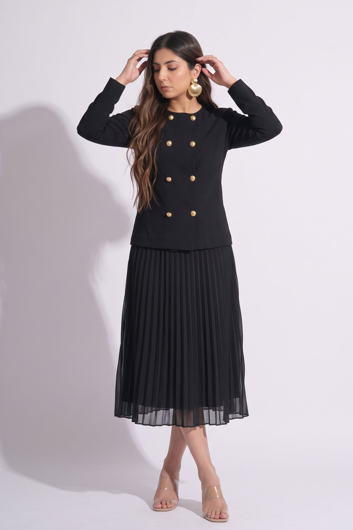 Woman wearing a black outfit with a jacket and pleated skirt on a white background