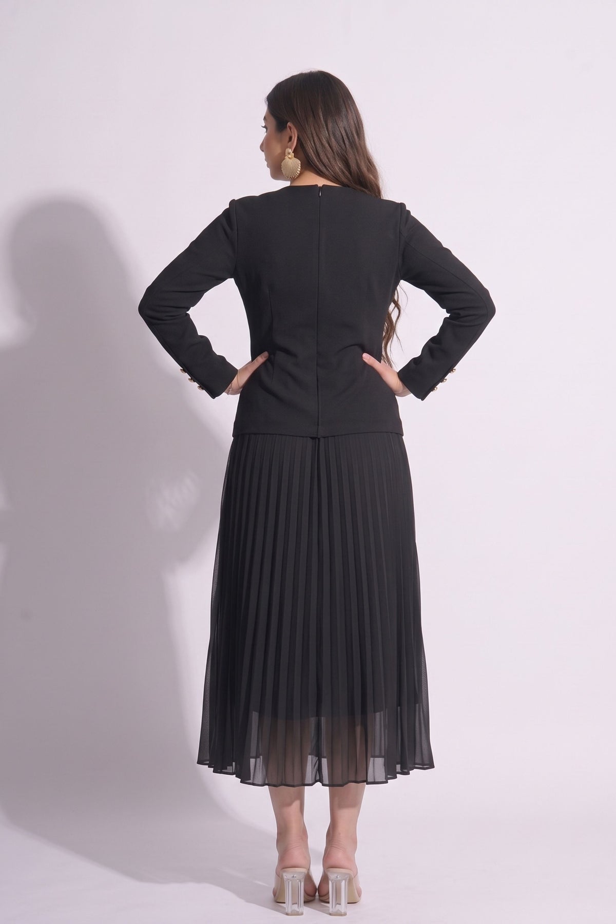 Woman wearing a black outfit with a jacket and pleated skirt on a white background