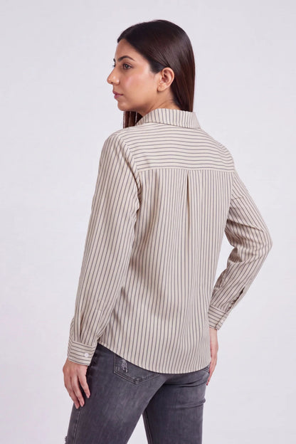 A woman shown from the back wearing a beige and white vertically striped long-sleeve blouse with dark gray jeans, photographed against a light gray studio background.