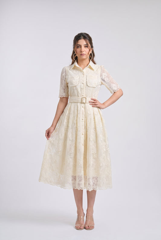 A woman modeling a cream-colored lace midi dress with short sleeves, a button-up front, and a matching fabric belt with a gold-tone buckle, set against a plain light gray studio background.
