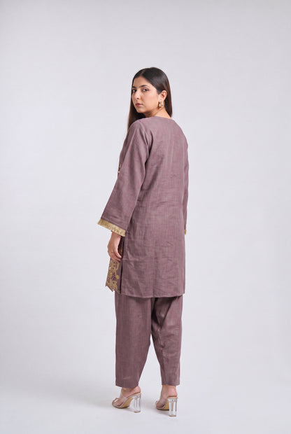 A woman modeling a two-piece dusty mauve kurta and trouser set, shown from a rear three-quarter angle against a light gray studio background.