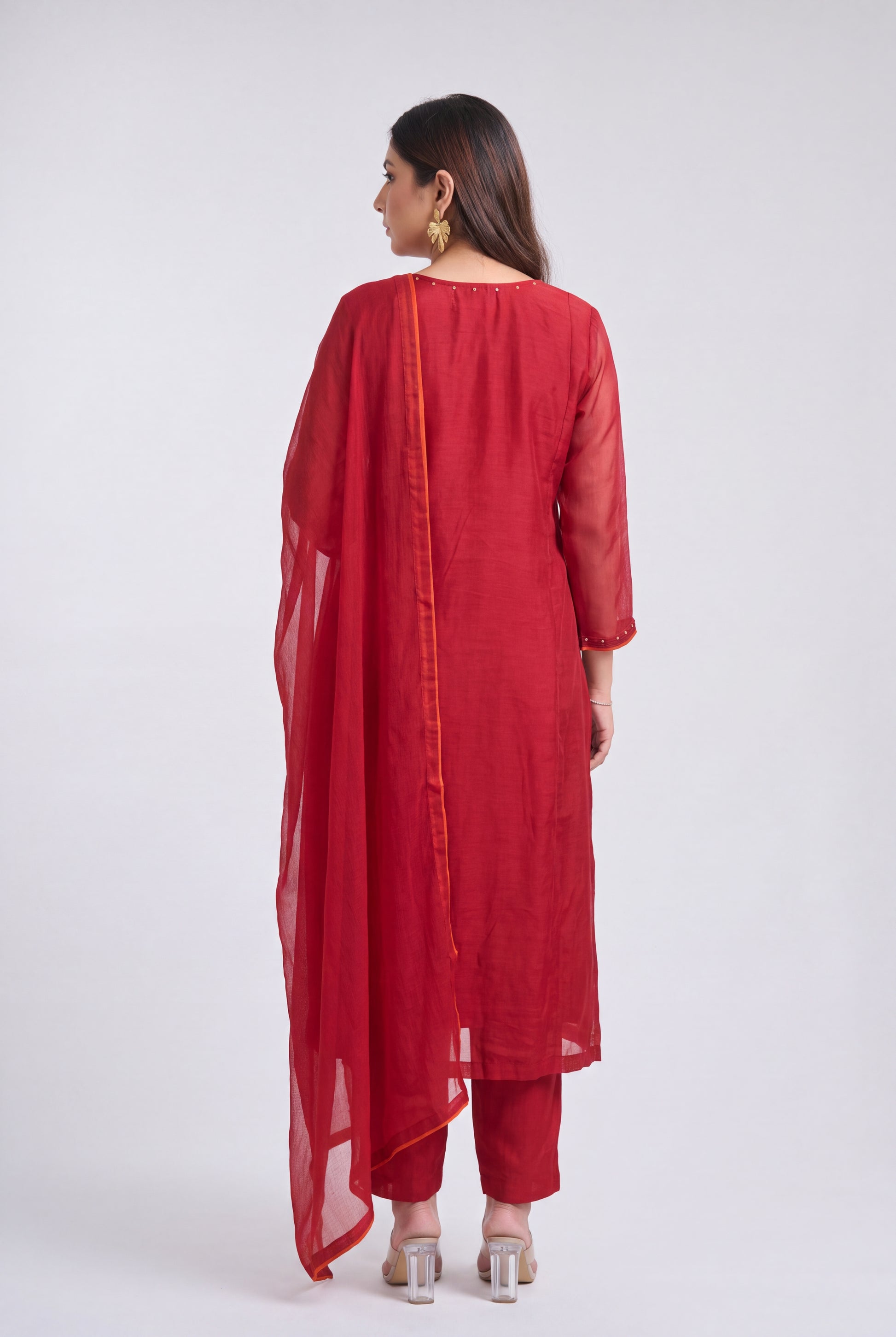A woman shown from the back wearing a red traditional outfit with matching pants and a sheer red dupatta, photographed against a plain light gray studio background.