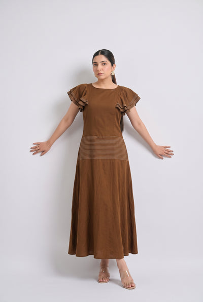 A woman modeling a brown maxi dress with ruffled short sleeves and a textured horizontal band at the waist, standing against a light gray studio background.