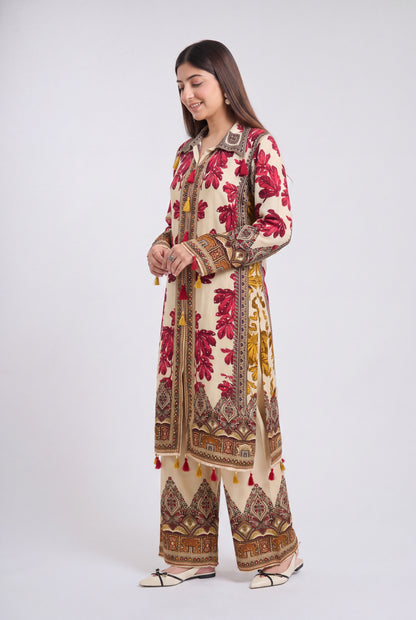 A woman modeling a traditional South Asian outfit consisting of a long cream-colored kurta and matching wide-leg trousers, decorated with red floral patterns and brown geometric borders, set against a plain light gray background.