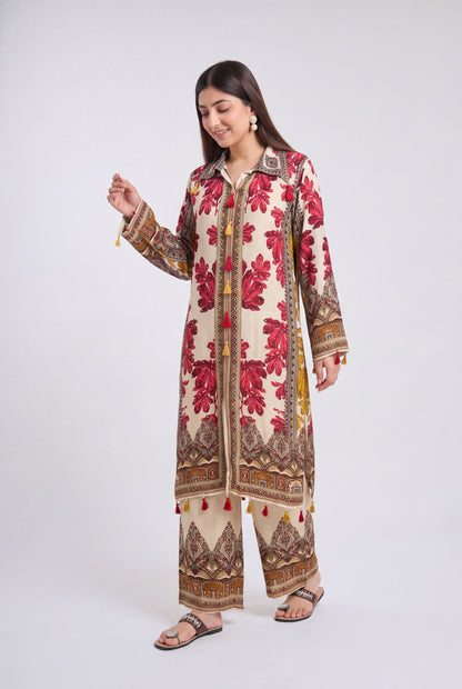 A woman modeling a traditional South Asian outfit consisting of a long cream-colored kurta with red floral embroidery and brown patterns, paired with matching wide-leg trousers, against a light gray studio background.