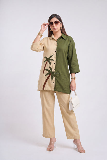 A woman models a two-tone button-up shirt and matching wide-leg trousers. The shirt is split vertically with one side in beige featuring a green palm tree print and the other side in olive green.