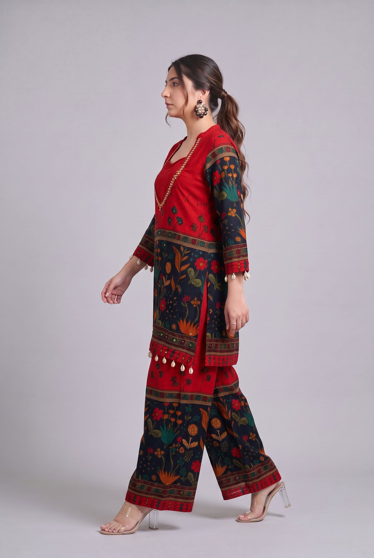 A woman modeling a red and black printed traditional outfit with floral patterns, shown in profile against a light gray studio background.