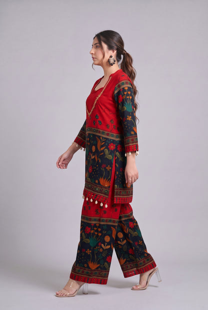 A woman modeling a red and black printed traditional outfit with floral patterns, shown in profile against a light gray studio background.
