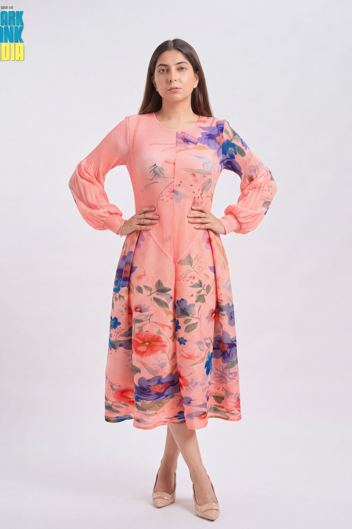 A woman modeling a peach pink long-sleeve kurta with a colorful floral print, standing against a light gray studio background.