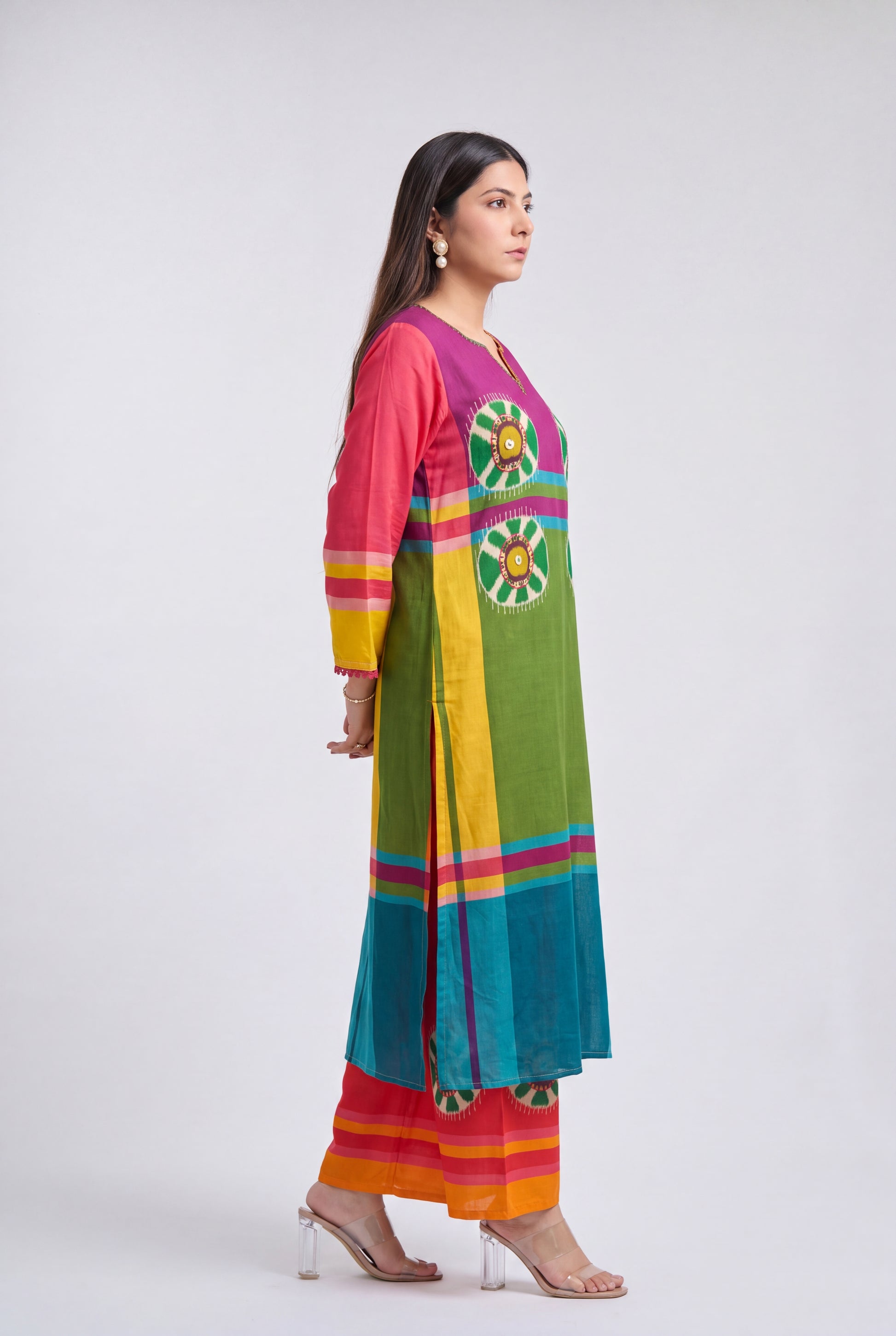 A woman modeling a vibrant, multicolored traditional Indian kurta set with matching pants. The kurta features a bright green body with yellow and pink stripes, a magenta collar, and green and yellow floral embroidery on the chest.