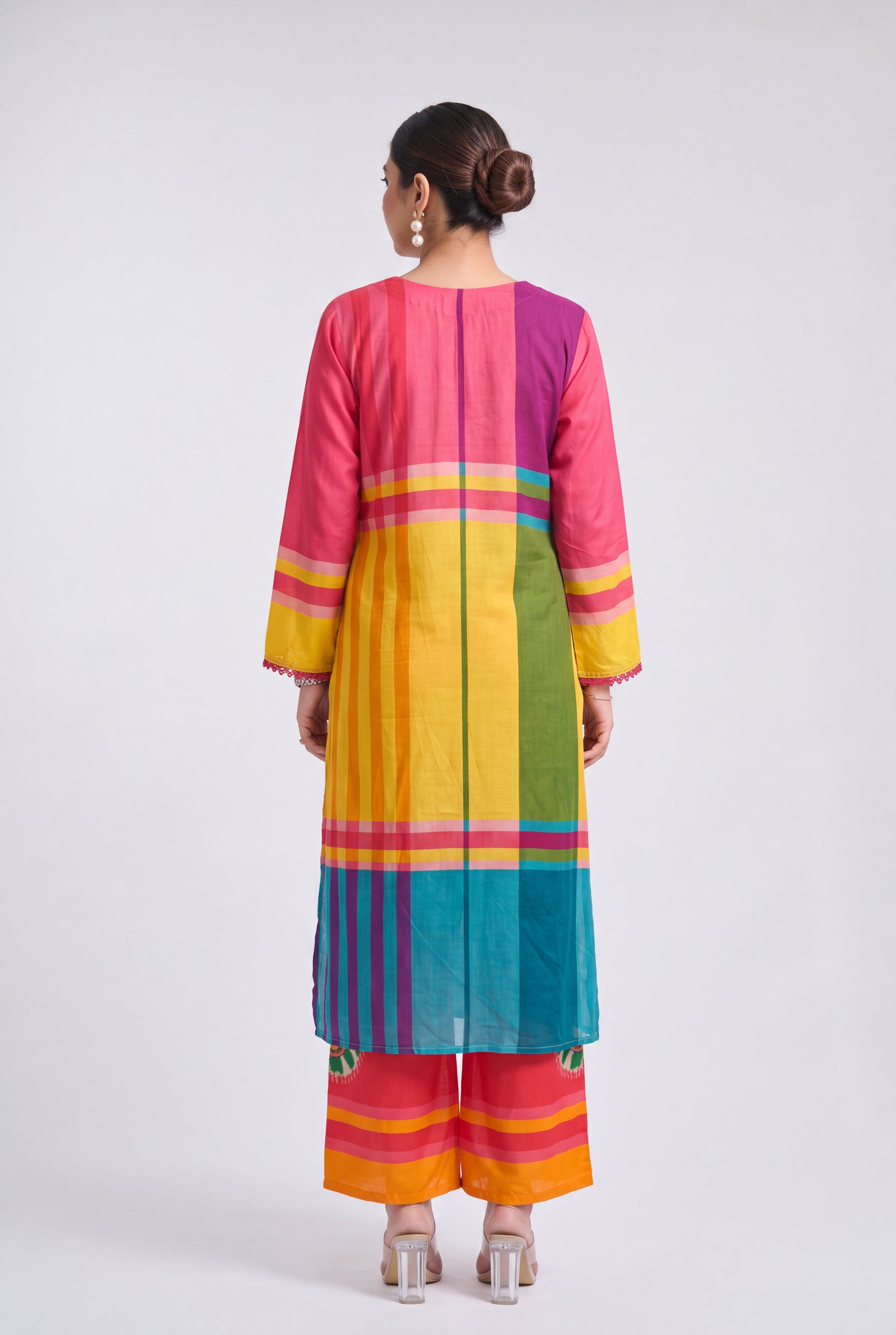 A woman viewed from the back wearing a brightly colored striped kurta and matching wide-leg pants. The outfit features vertical panels of pink, purple, yellow, green, blue, orange, and red with thin horizontal accent stripes, set against a plain light gray studio background.