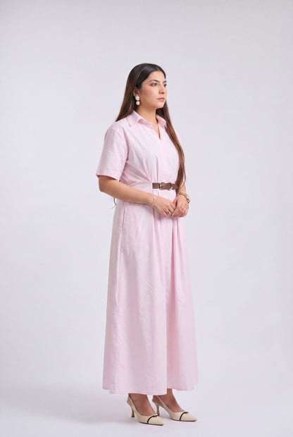 A woman modeling a light pink short-sleeve collared maxi dress with a matching belt, standing against a plain light gray studio background.