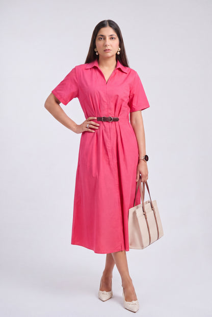 A woman models a short-sleeve pink midi shirt dress with a black belt, holding a beige tote bag and wearing beige heels, against a light gray studio background.