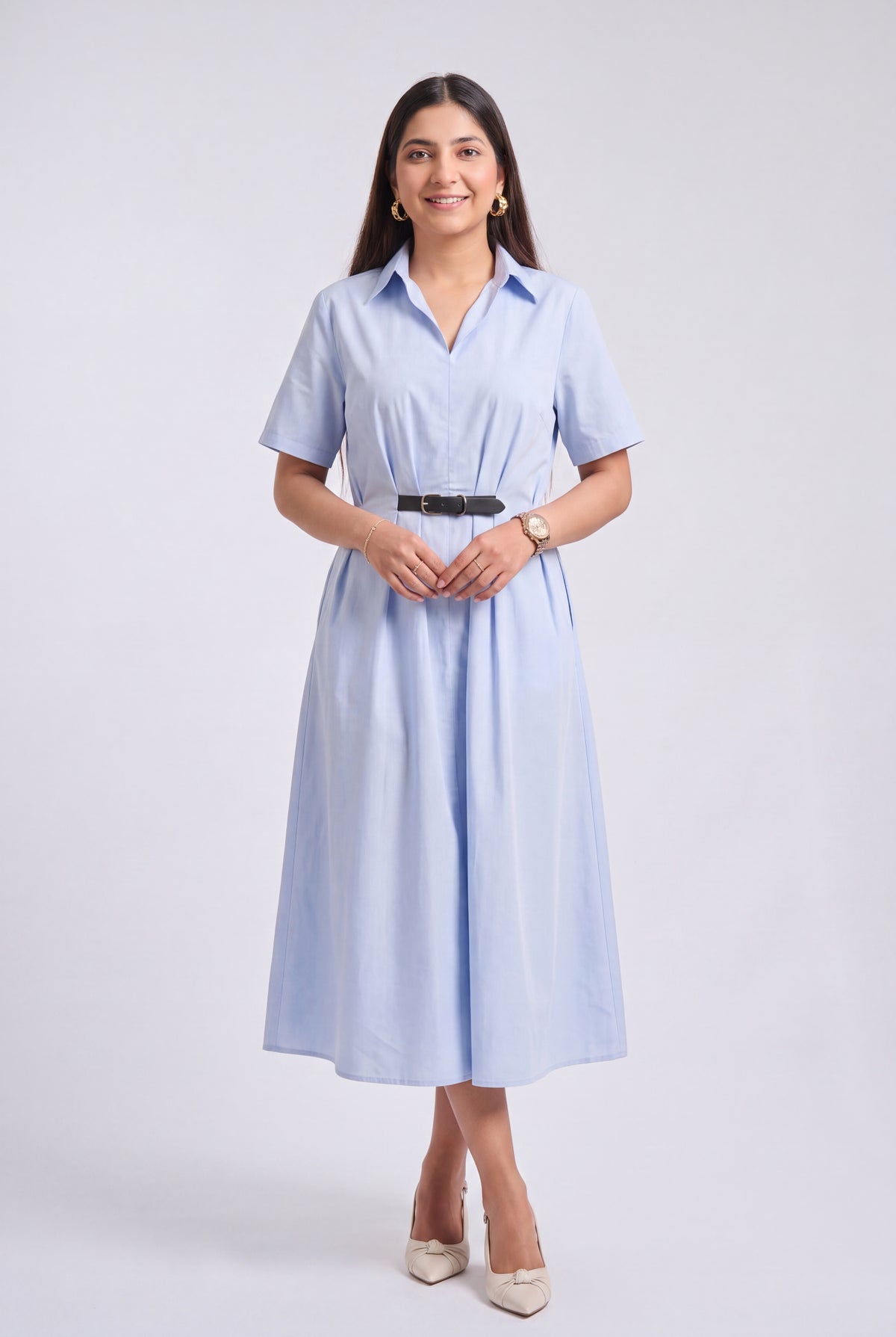 A woman modeling a light blue short-sleeve midi shirt dress with a black belt, standing against a light gray studio background.