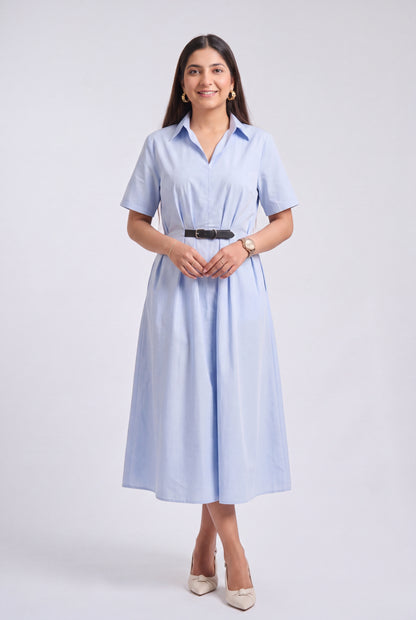 A woman modeling a light blue short-sleeve midi shirt dress with a black belt, standing against a light gray studio background.