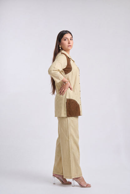 A woman modeling a beige two-piece kurta set with brown contrast panels, shown in profile against a light gray studio background.
