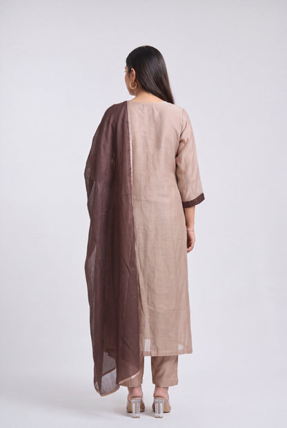 A woman shown from the back wearing a light beige straight kurta with dark brown trim, matching beige pants, and a dark brown dupatta, set against a plain light gray studio background.