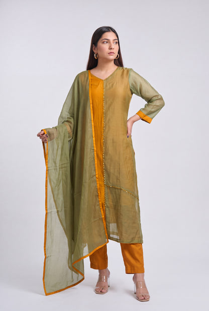 A woman modeling a traditional Indian outfit consisting of an olive green kurta with gold embroidery, orange pants, and a matching olive green dupatta with an orange border, set against a plain light gray background.