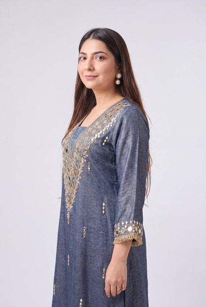 A woman modeling a slate blue kurta with gold mirror work embroidery on the neckline and cuffs, set against a plain light gray background.