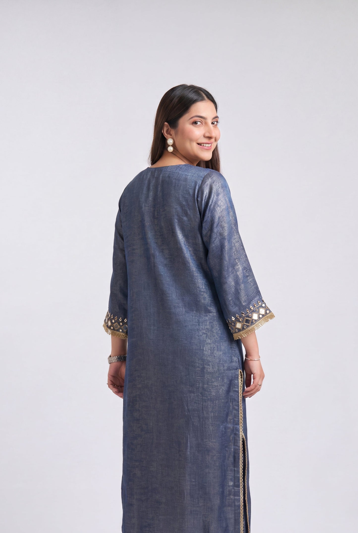 A woman modeling a long blue-gray kurta with gold embroidered details on the cuffs and hem, shown from the back against a light gray studio background.