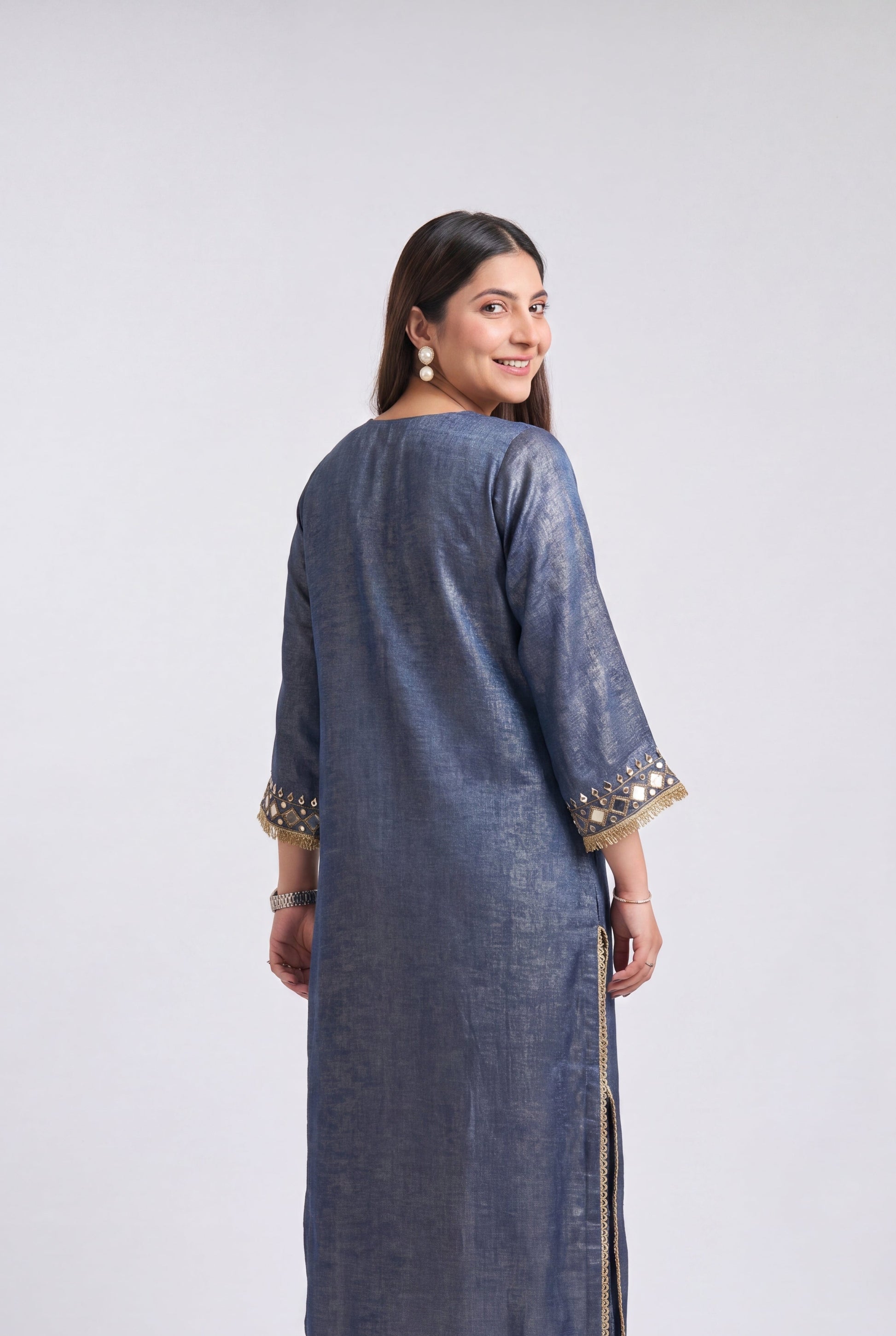 A woman modeling a long blue-gray kurta with gold embroidered details on the cuffs and hem, shown from the back against a light gray studio background.