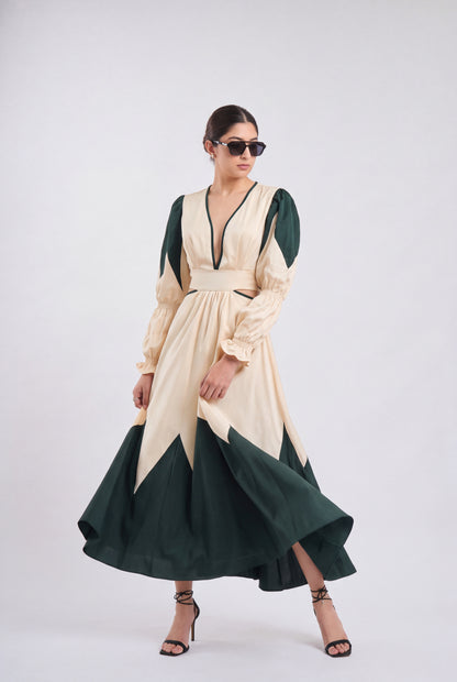 A woman modeling a long-sleeved midi dress with a cream and dark green color-blocked design, featuring a V-neckline, puffed sleeves, and a flared skirt, set against a plain light gray studio background.