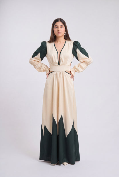 A woman modeling a long cream maxi dress with dark green color-blocked sleeves, neckline trim, and hem details, standing against a light gray studio background.