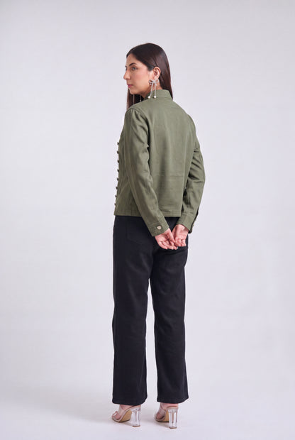 A woman modeling an olive green military-style jacket with silver buttons, paired with black wide-leg pants and clear high-heeled sandals, against a light gray studio background.