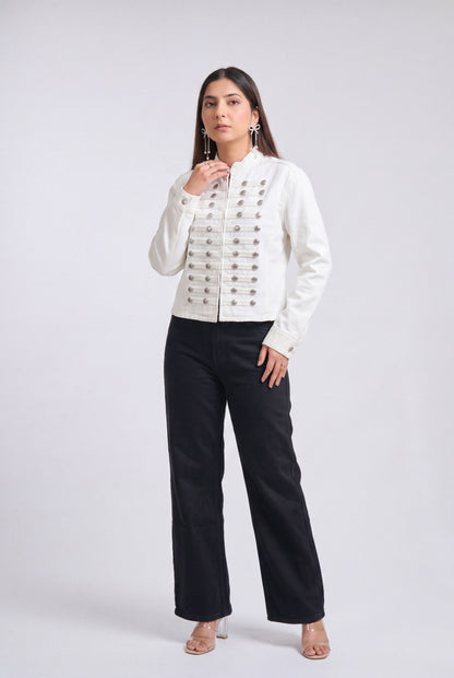 A woman modeling a white cropped jacket with ornate silver button detailing down the front, paired with black wide-leg trousers, against a light gray studio background.