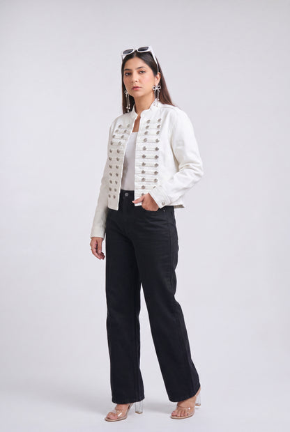 A woman modeling a white cropped jacket with ornate silver button detailing down the front, paired with black wide-leg trousers, against a light gray studio background.