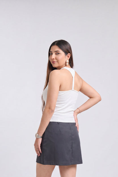 A woman modeling a dark gray mini skirt paired with a white tank top, standing against a light gray studio background.