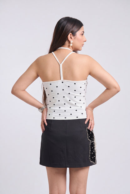 A woman shown from the back wearing a white halter top with black polka dots and a black mini skirt with a black beaded side detail, against a light gray studio background.
