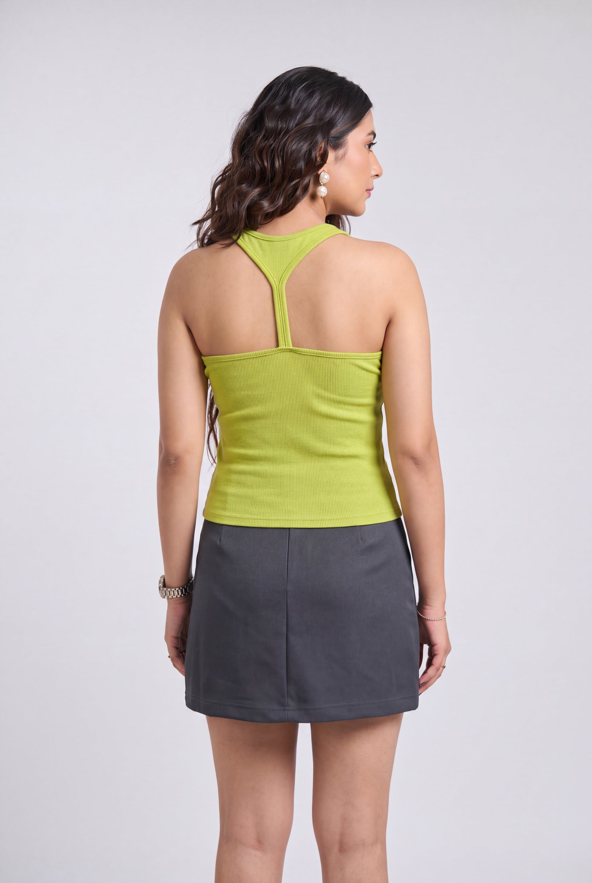 A woman shown from the back wearing a lime green halter-neck top and a dark gray mini skirt, photographed against a light gray studio background.