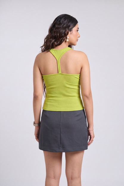 A woman shown from the back wearing a lime green halter-neck top and a dark gray mini skirt, photographed against a light gray studio background.