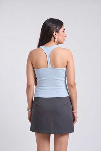 A woman shown from the back wearing a light blue ribbed tank top with a crossover back design and a dark gray mini skirt, set against a plain light gray studio background.
