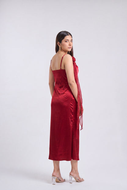 A woman modeling a deep red satin slip dress with thin straps and a draped sheer red shawl, photographed against a neutral light gray studio background.