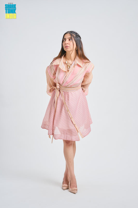A woman modeling a light pink and white striped wrap dress with sheer peach sleeves and a beige belt, standing against a light gray studio background. A 'Think Tank India' logo is visible in the top left corner.