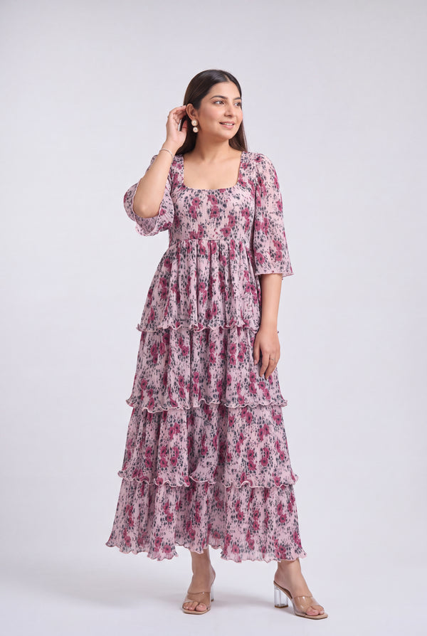 A woman shown from the wearing a tiered maxi dress with a pink and purple floral print on a white base, photographed against a light gray studio background.